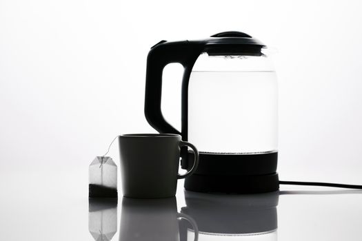 Electric kettle with clear water beside a mug for descaling