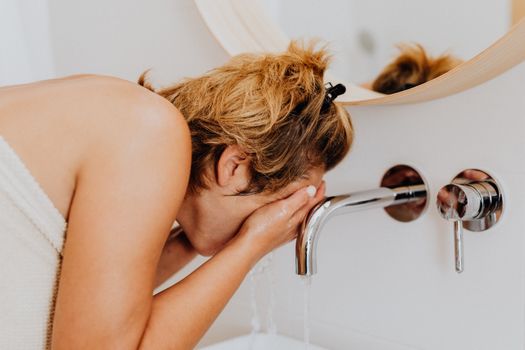 Woman splashing water on her face as part of a skincare routine