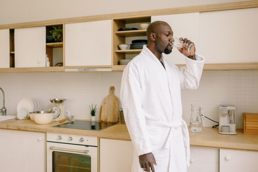 Person in a bathrobe drinking a glass of water in the kitchen before coffee