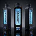 Hero marketing trio of three black rectangular Dr.Water Hydrator Max hydrogen water bottles in a row on a glossy reflective surface against a dark charcoal gradient studio backdrop; the centre bottle has a brightly glowing blue water window while the flanking bottles show subdued lighting variants, with the dr.water wordmark on each bottle window and small touchscreen icons on the base.