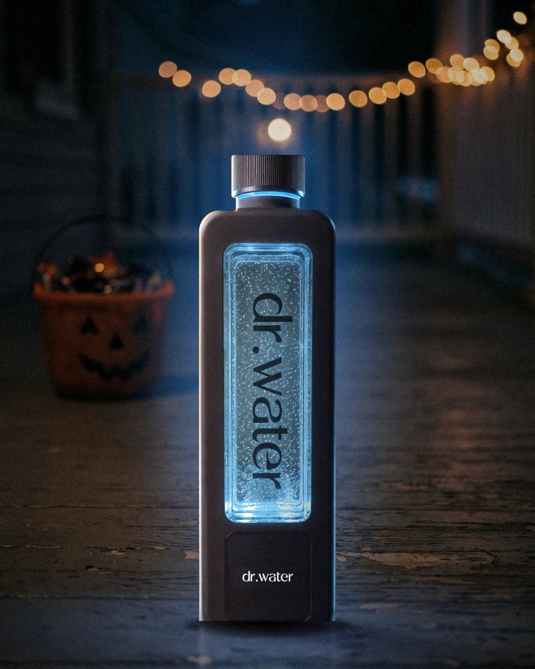 Dr.Water Hydrator Max hydrogen water bottle with its glowing blue water window on a Halloween porch at dusk, a jack-o'-lantern pail softly out of focus behind
